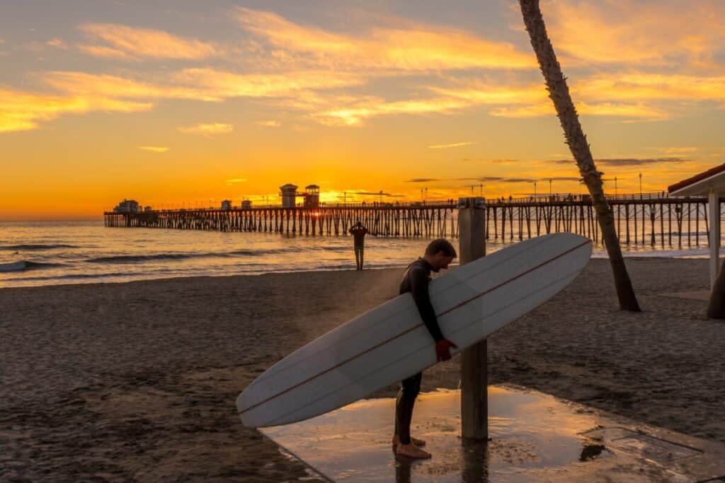 Man with surfboard showering at public beach